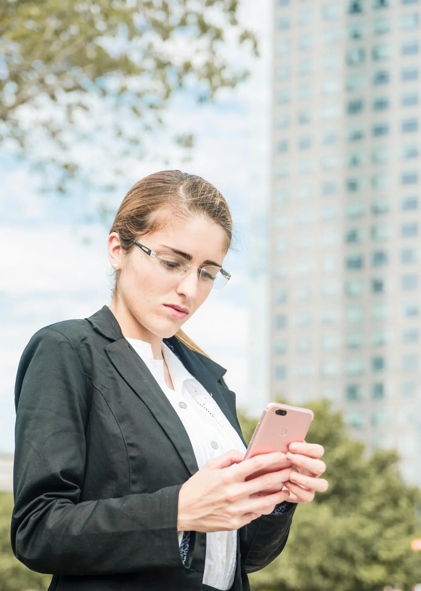 Mujer de negocios joven y seria con gafas usando un teléfono móvil.